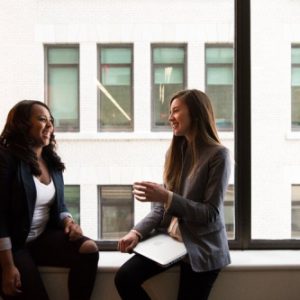 Two women casually talking in front of a window