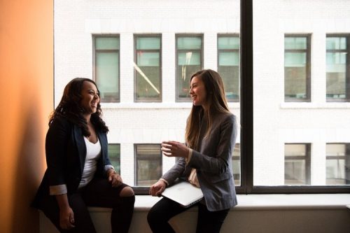 Two women casually talking in front of a window