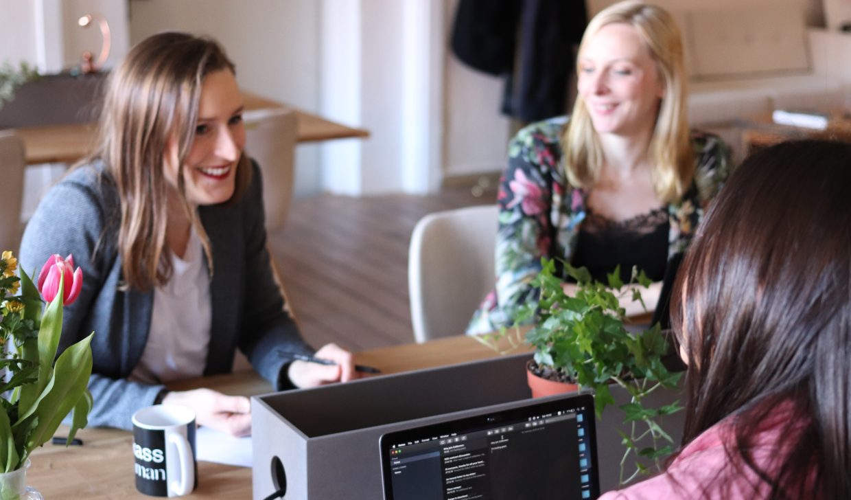 Three women speaking around a table with laptops with code