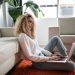 Woman sitting on the floor leaning against a couch working on her laptop